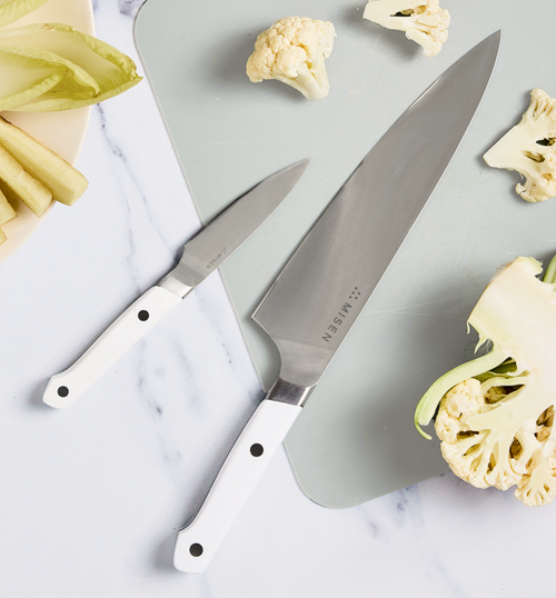 Misen chef's knife and paring knife with white handles on cutting board with cauliflower