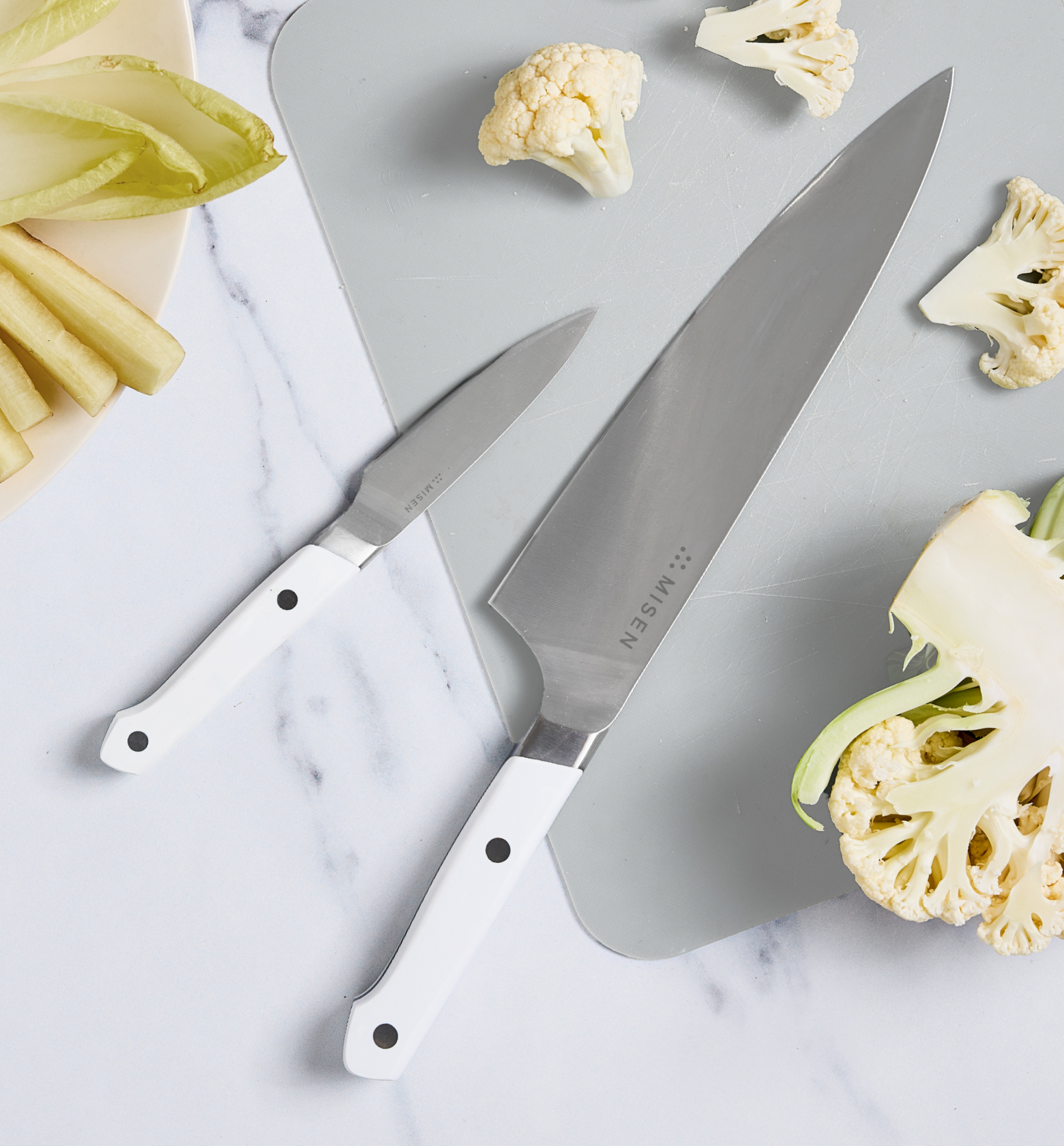 Misen chef's knife and paring knife with white handles on marble surface with cauliflower